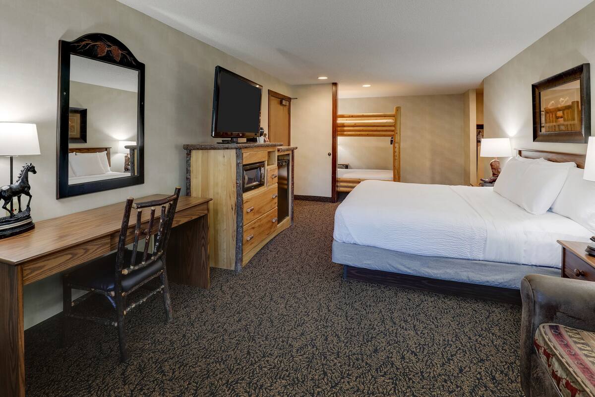 A hotel room with a bed, a desk with a chair, a television, and a mirror.