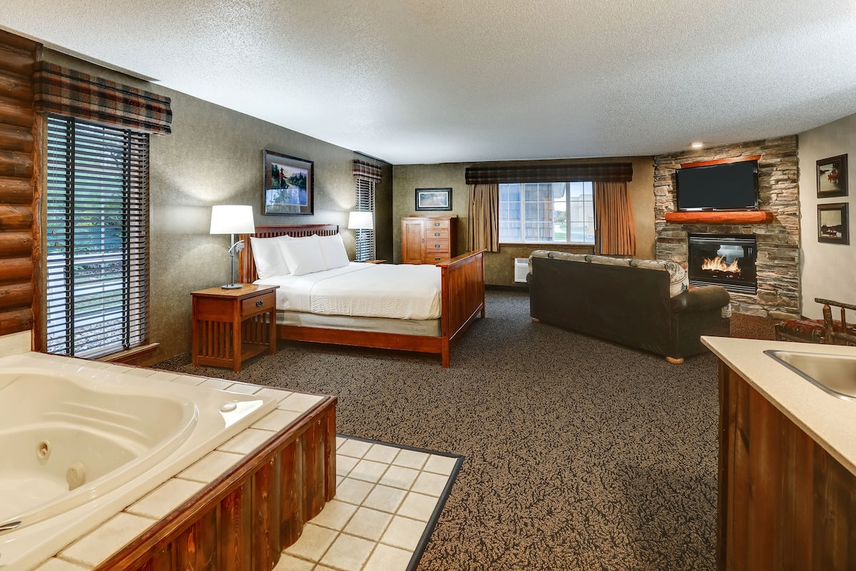 A hotel room with a large bed, a fireplace, a TV, and a jacuzzi.