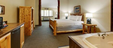 A hotel room with a wooden bed, a large bathtub, a wooden desk with a dishwasher, and a ceiling fan.