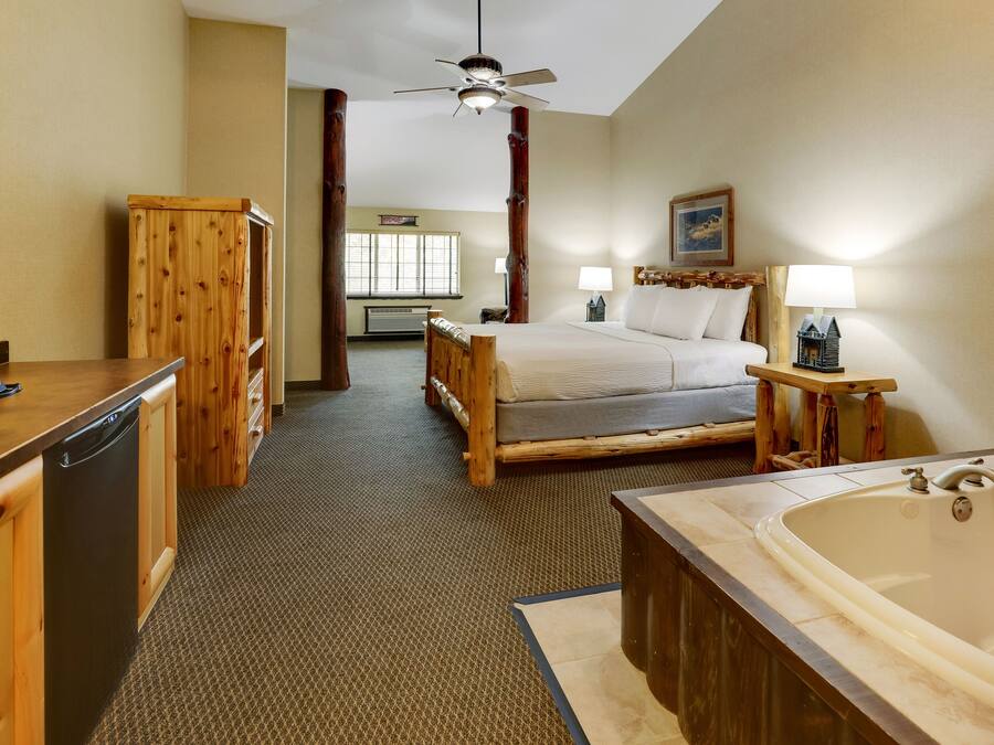 Een hotelkamer met een houten bed, een groot bad, een houten bureau met een vaatwasser en een plafondventilator.