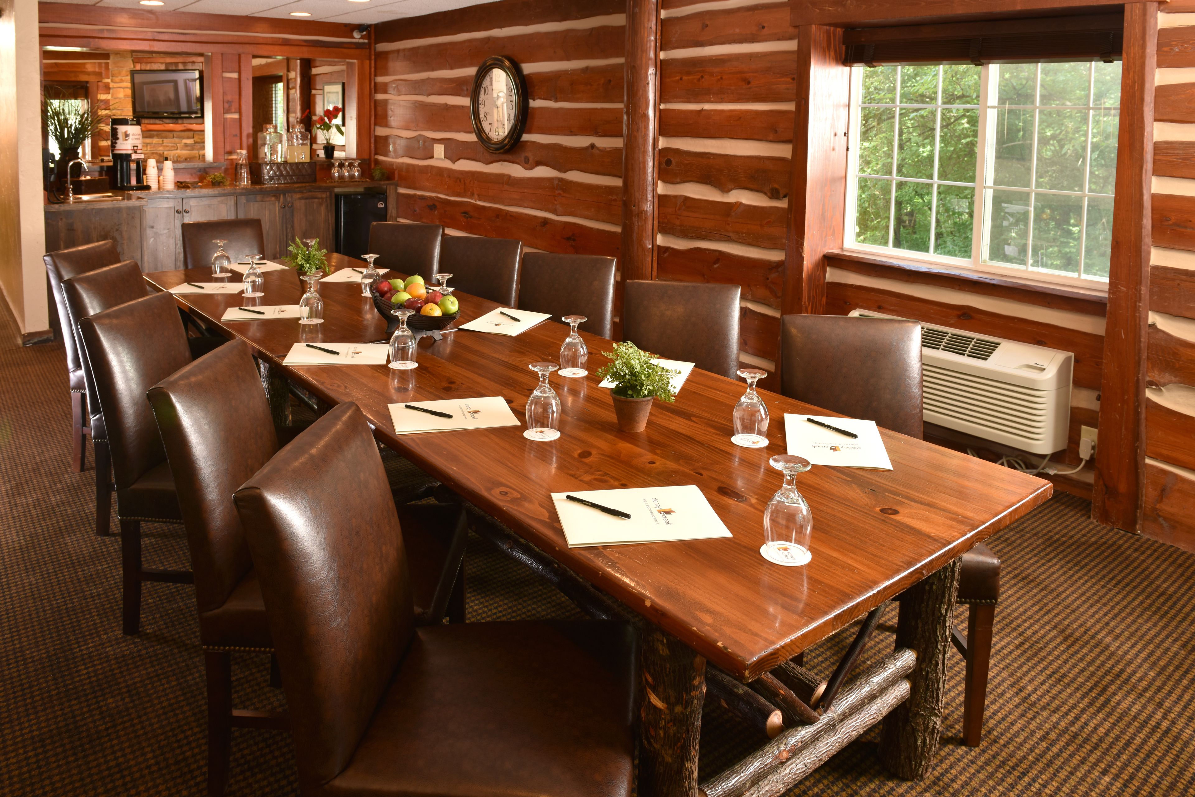 A conference room with a long wooden table, leather chairs, and a clock on the wall.
