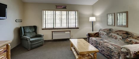 A living room with a green leather chair, a wooden table, a patterned sofa, and a window with blinds.