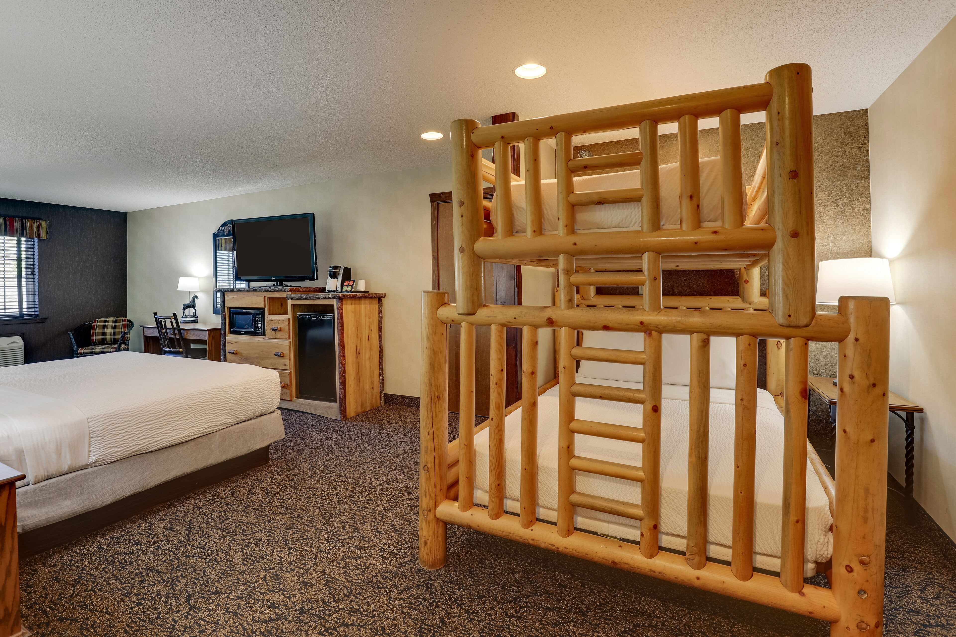 A hotel room with a bunk bed, a desk with a computer, a television, and a lamp.