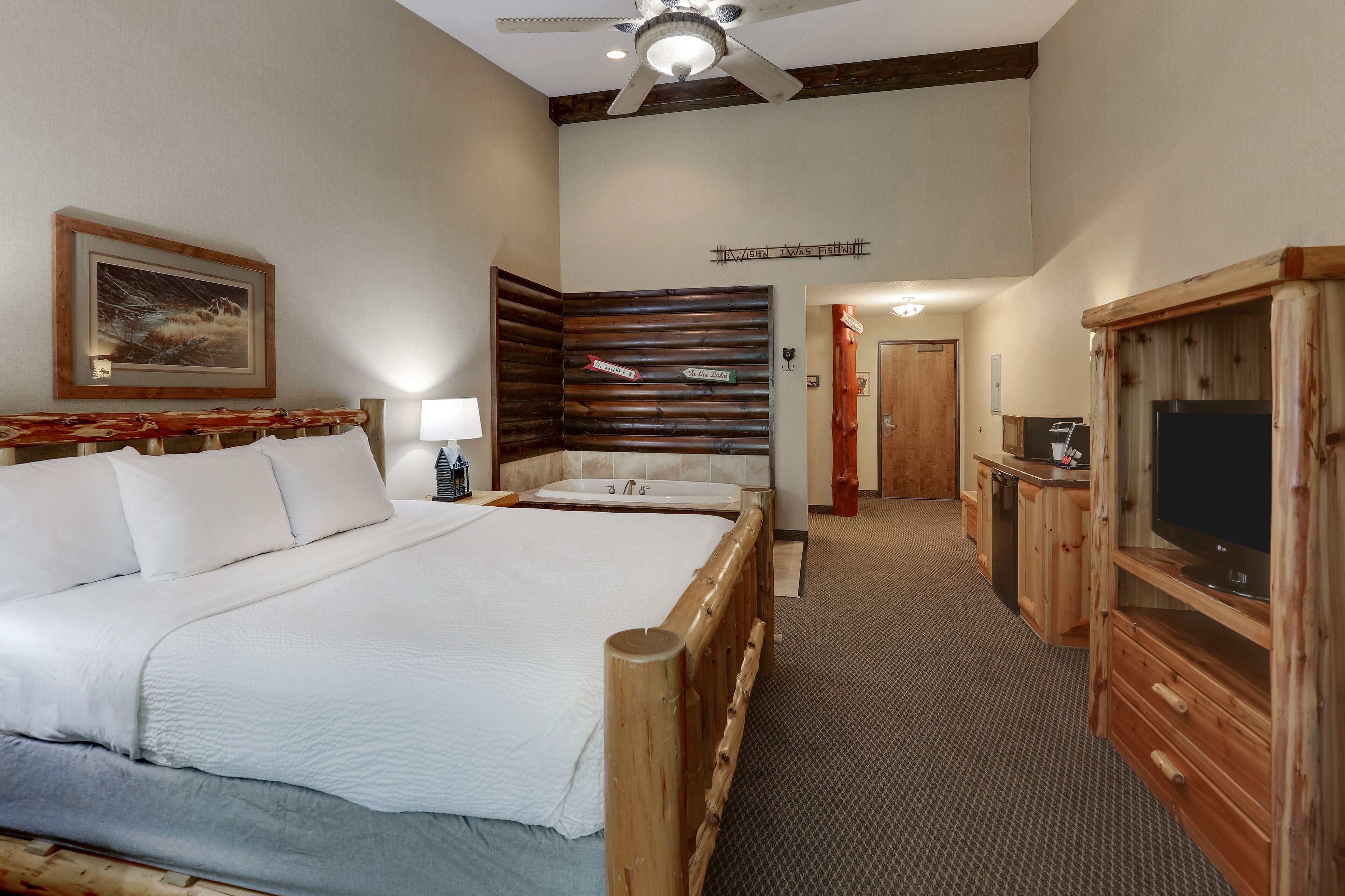 A hotel room with a large bed, a wooden headboard, a television, and a bathroom with a bathtub.