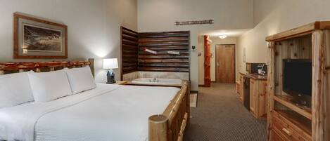 A hotel room with a large bed, a wooden headboard, a television, and a bathroom with a bathtub.