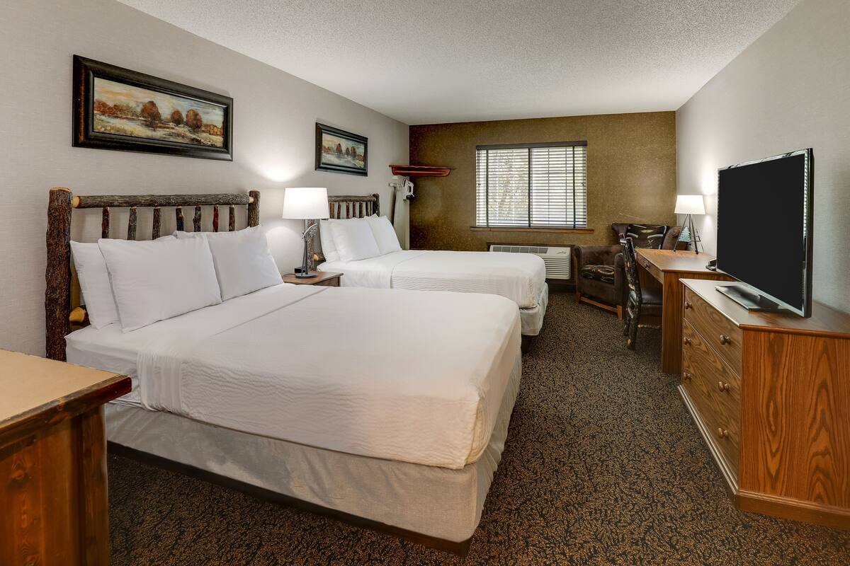 A hotel room with two beds, a desk, a television, and a window with blinds.