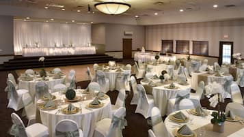 Un salón de banquetes con mesas redondas preparadas para un evento formal, con manteles blancos, detalles dorados y centros de mesa florales.