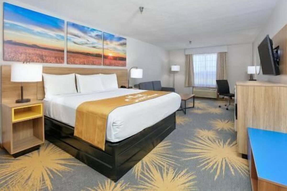 A hotel room with a bed, bedside tables, a desk, a chair, a TV, and artwork on the wall.