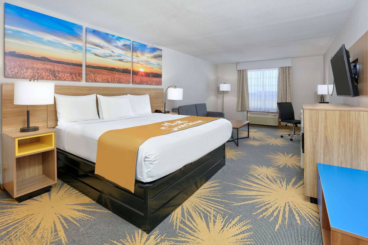 A hotel room with a bed, bedside tables, a desk, a chair, a TV, and artwork on the wall.