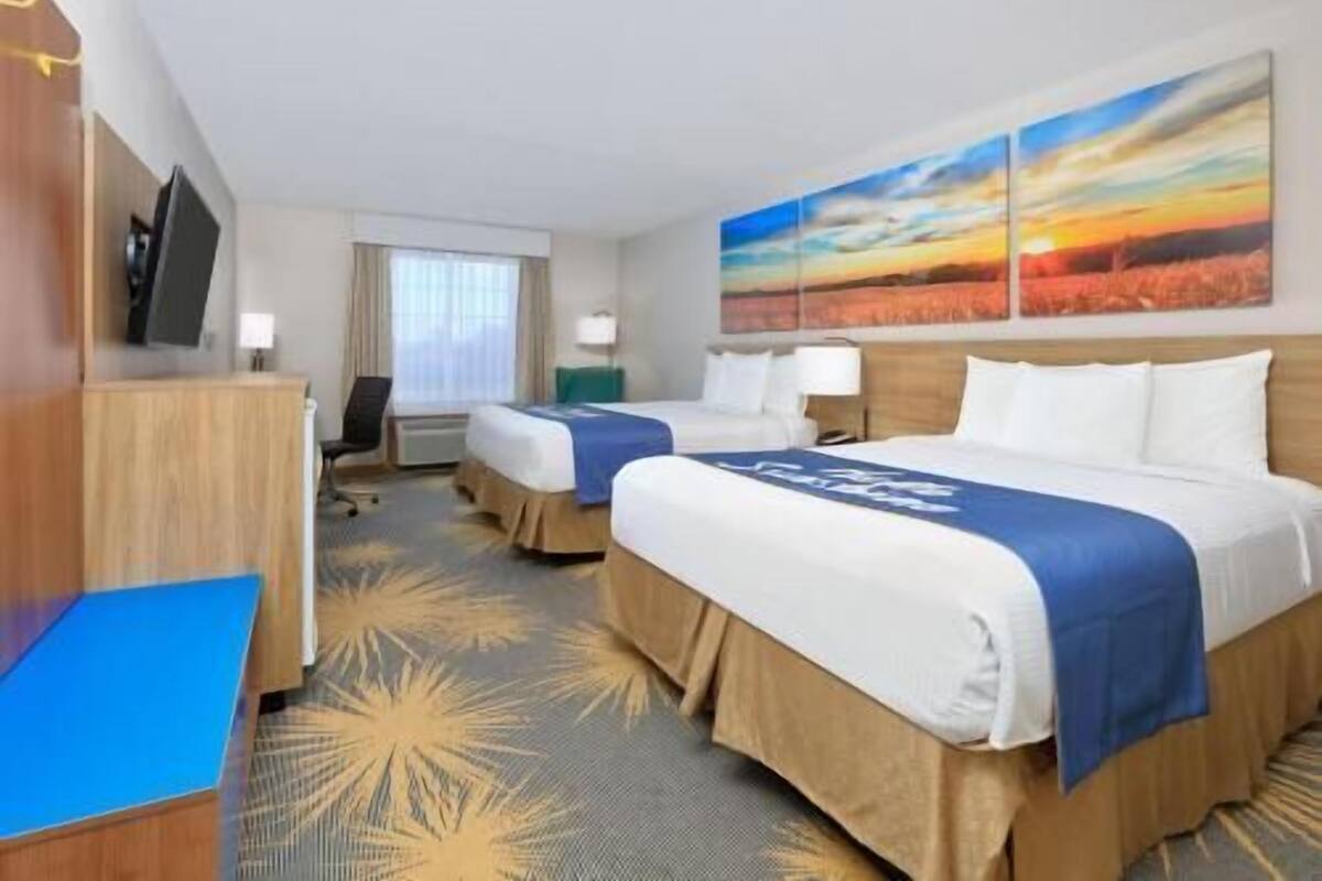 A hotel room with two beds, a desk, a chair, a TV, and a painting of a sunset.