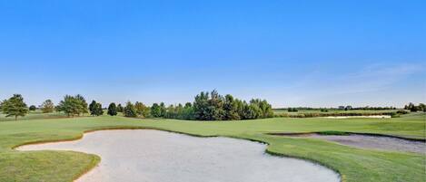 Un campo de golf con búnkeres de arena y árboles al fondo.