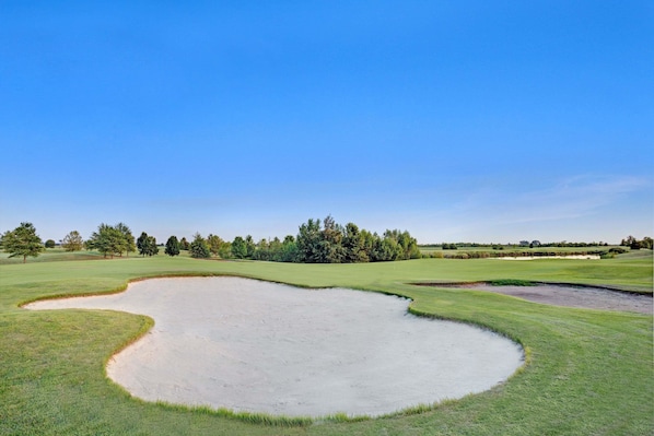 A golf course with sand bunkers and trees in the background.