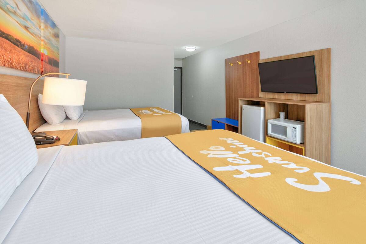 A hotel room with two beds, a television, a microwave, and a painting on the wall.