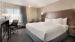 A hotel room with a large bed, a desk with a lamp, a chair, and a nightstand. - Baymont by Wyndham Des Moines North (Des Moines)