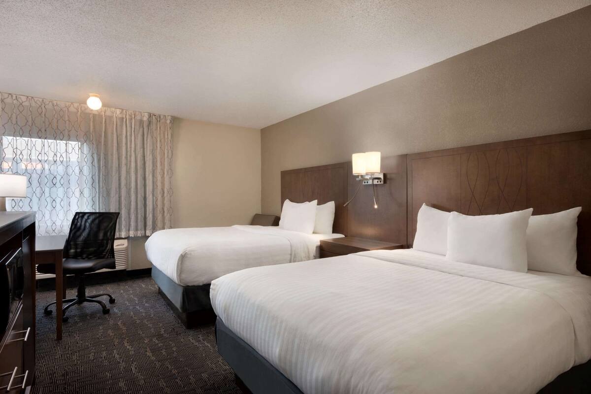 Une chambre d’hôtel avec deux lits, un bureau, une chaise et une fenêtre avec des rideaux.