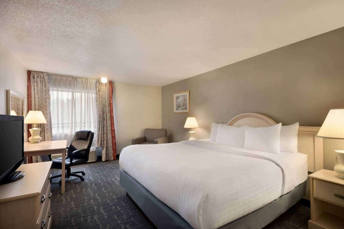 Une chambre d’hôtel avec un grand lit, un bureau avec un ordinateur, une chaise et deux lampes de chevet.