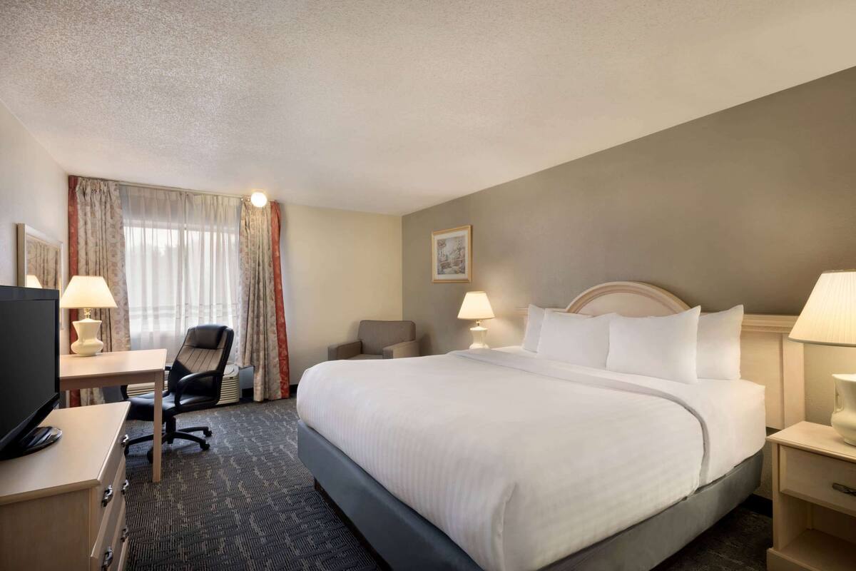 Une chambre d’hôtel avec un grand lit, un bureau avec un ordinateur, une chaise et deux lampes de chevet.