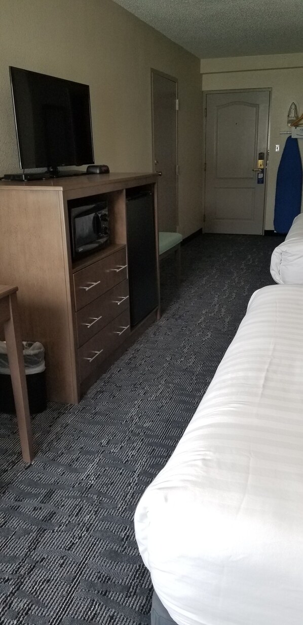A hotel room with a bed, a desk with a television, a microwave, and a door.