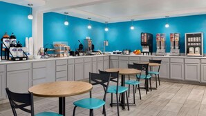 A modern kitchen with blue walls, a counter with coffee machines, and seating for four. - Baymont by Wyndham Des Moines North (Des Moines)