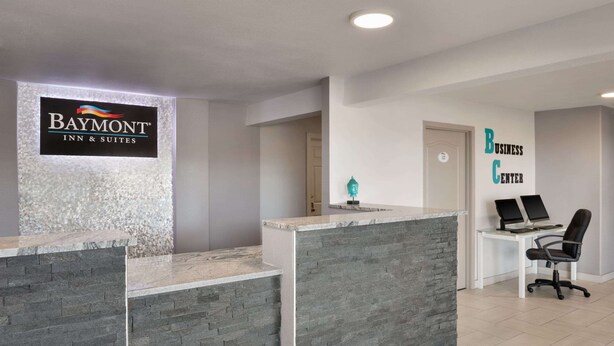 A reception area with a Baymont Inn & Suites sign, a business center, and a reception desk with a stone facade. - Baymont by Wyndham Des Moines North (Des Moines)