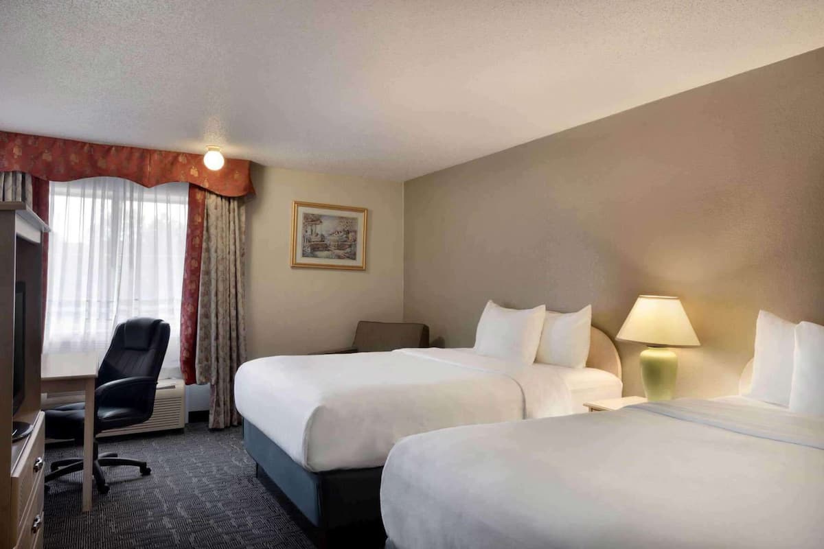 Une chambre d’hôtel avec deux lits, un bureau, une chaise, une lampe et un tableau au mur.