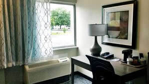 A hotel room with a desk, a chair, a lamp, a phone, a coffee maker, and a window with curtains. - Baymont by Wyndham Des Moines North (Des Moines)
