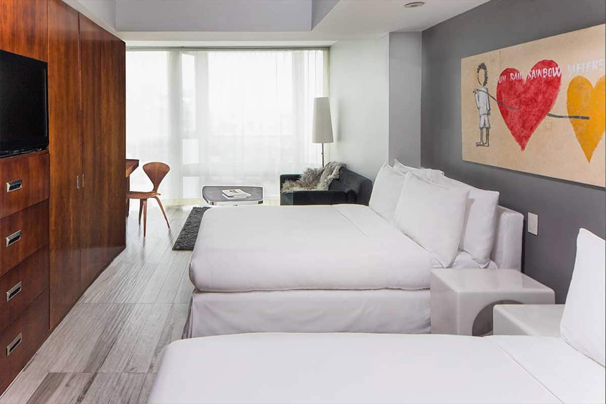 Quarto de hotel moderno com uma cama grande, televisão, escrivaninha e um quadro na parede.