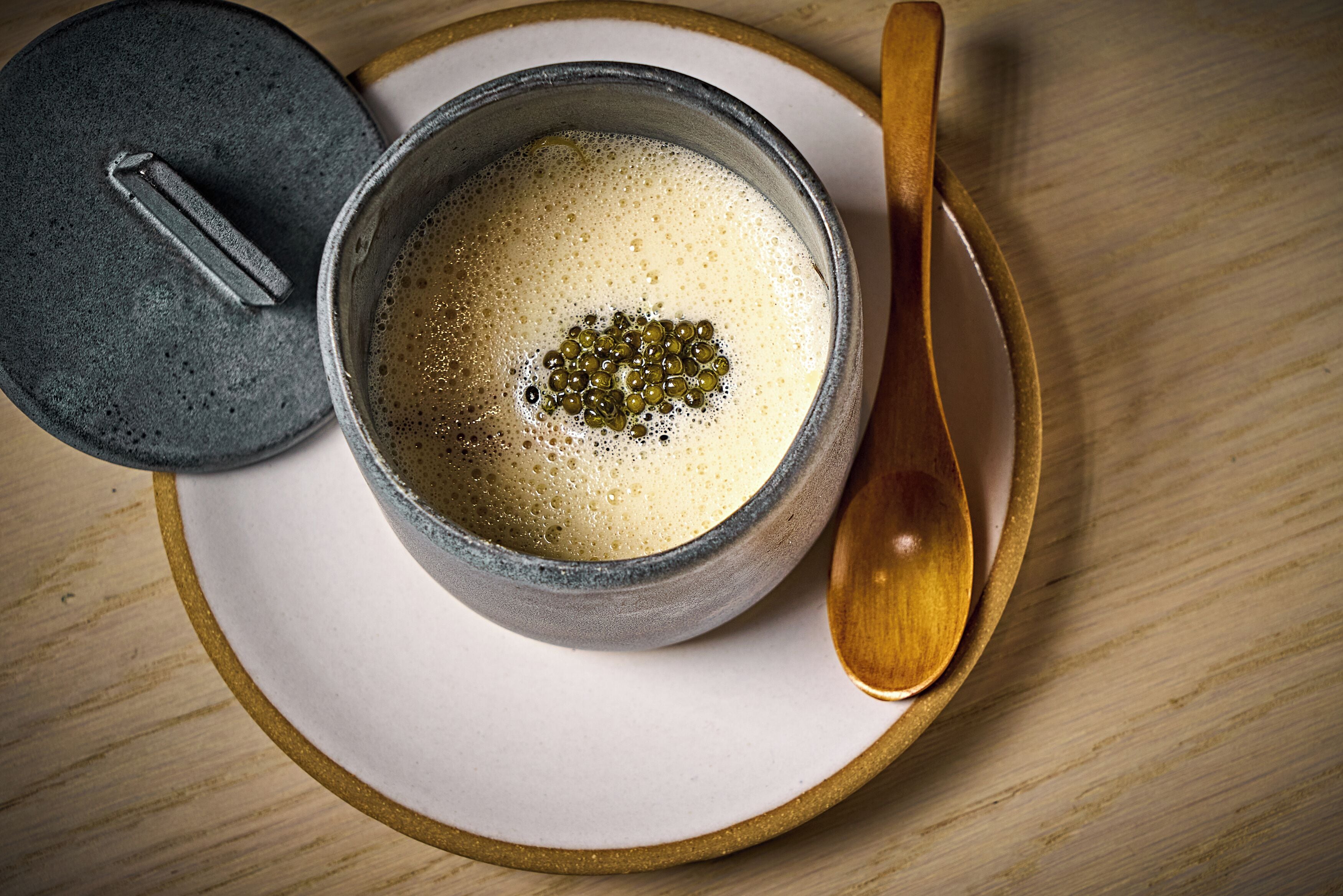 A cup of coffee with a spoon and a lid on a wooden table.