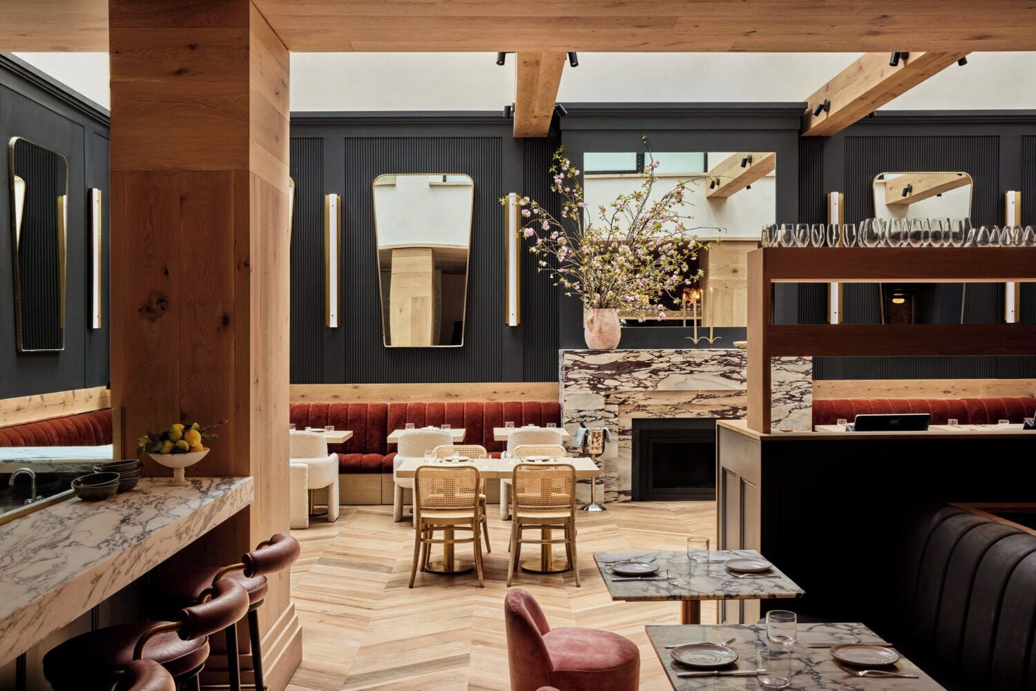 A modern restaurant interior with wooden beams, marble flooring, and a central fireplace.
