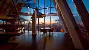 A modern interior with a panoramic city view, a dining area, and hanging light fixtures. - Hotel On Rivington (New York)