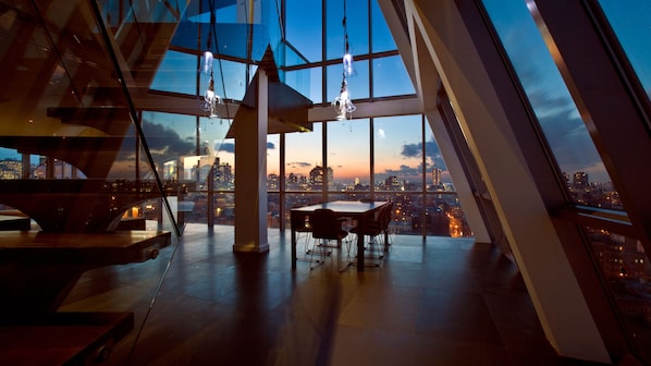 A modern interior with a panoramic city view, a dining area, and hanging light fixtures.