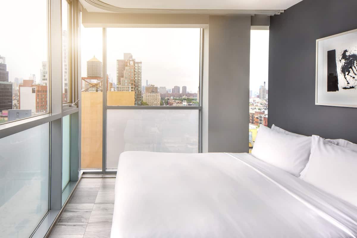Quarto de hotel moderno com uma cama grande, vista para a cidade e varanda.