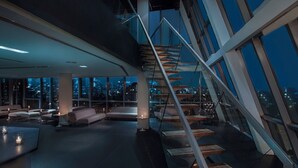A modern interior with a spiral staircase, seating areas, and large windows offering city views. - Hotel On Rivington (New York)