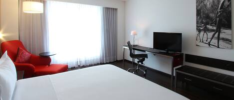 Une chambre d’hôtel avec un grand lit, un bureau avec une chaise, une télévision et un tableau au mur.