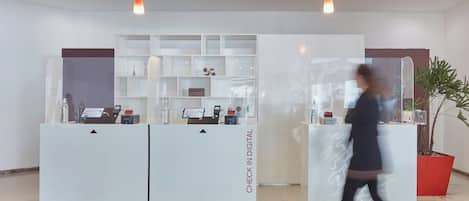 Zona de recepción con mostrador de registro digital, una planta en maceta y diseño interior moderno.