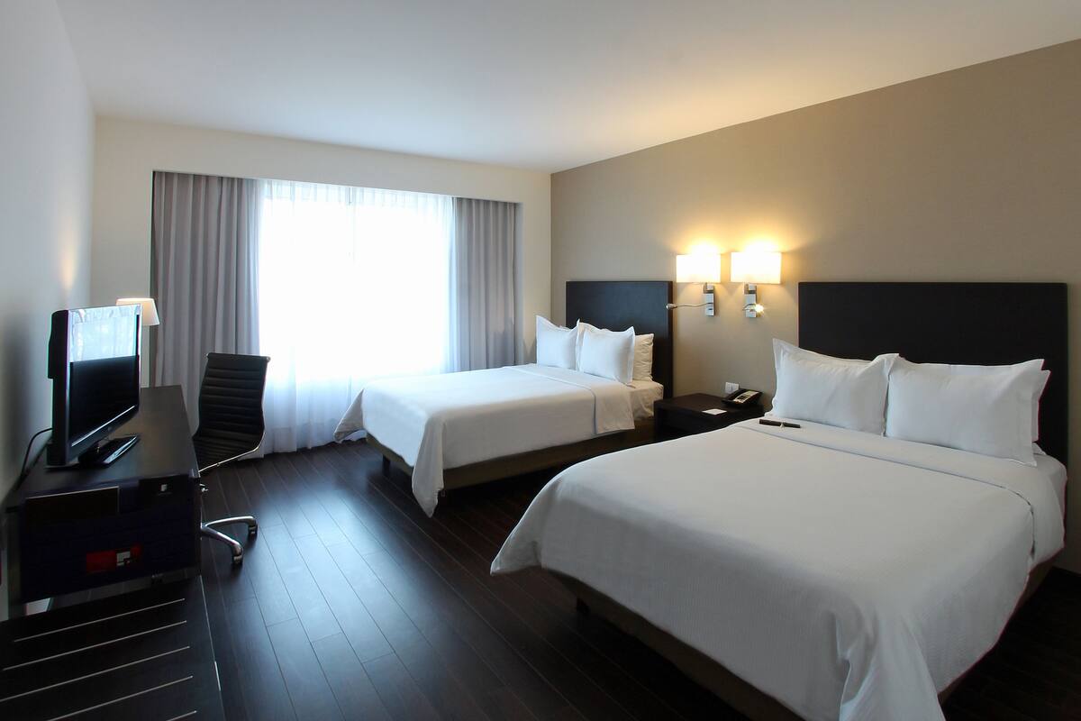 Una habitación de hotel con dos camas, un escritorio con ordenador y televisión.