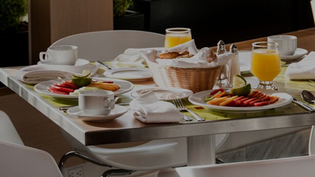 A breakfast table set with plates of food, glasses of orange juice, and a basket of pastries.