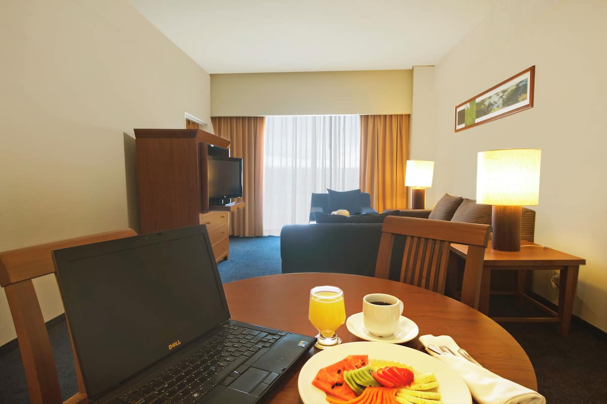 A hotel room with a laptop on a table, a plate of fruit, a glass of orange juice, and a cup of coffee.