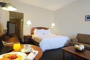 Hotelkamer met een bed, bedlampen, een bureau met een laptop, een eettafel met ontbijt en een bank.