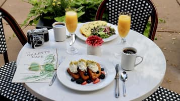 A round table with a menu, a camera, a plate of waffles with whipped cream and berries, two glasses of orange juice, and a cup of coffee.
