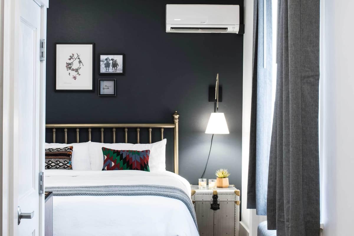 Un dormitorio con una cama, mesita de noche, lámpara, maleta y radiador.