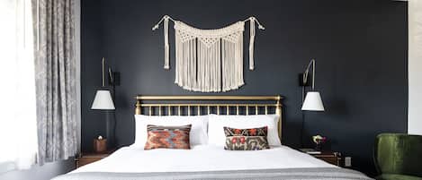 A neatly made bed with patterned pillows, a macrame wall hanging, and two bedside lamps.