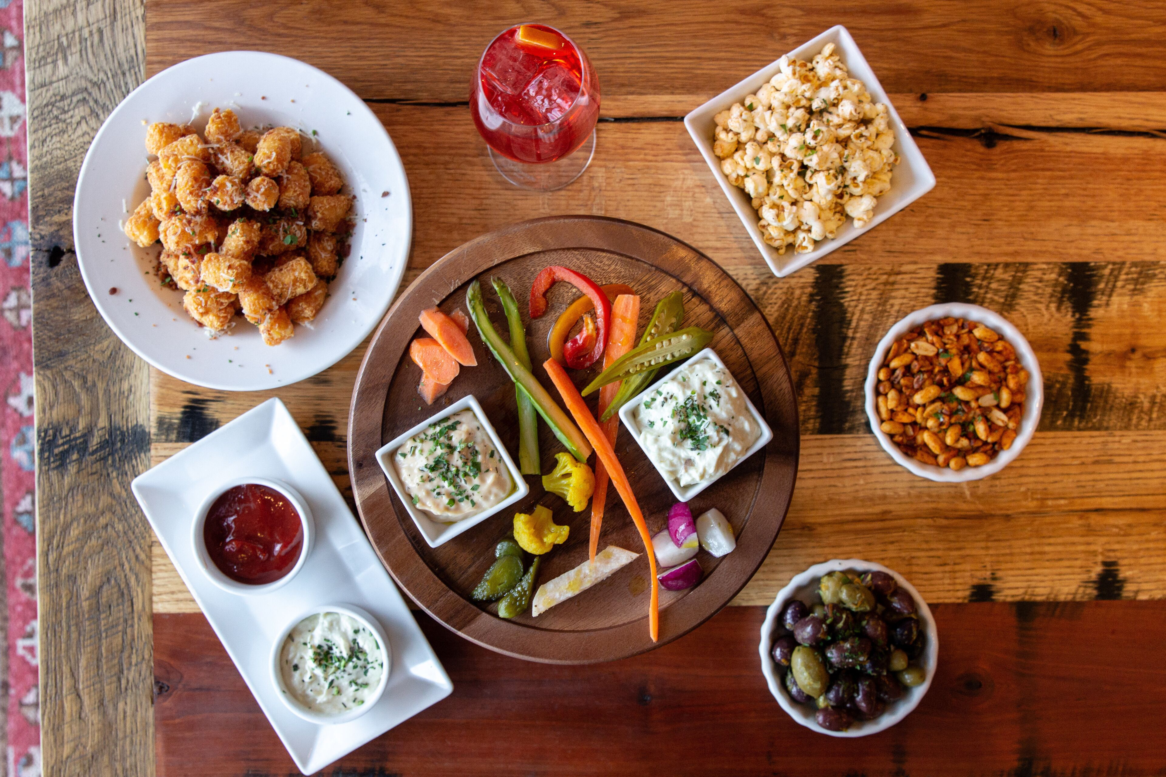A wooden table with a variety of food items including tater tots, popcorn, and dips.