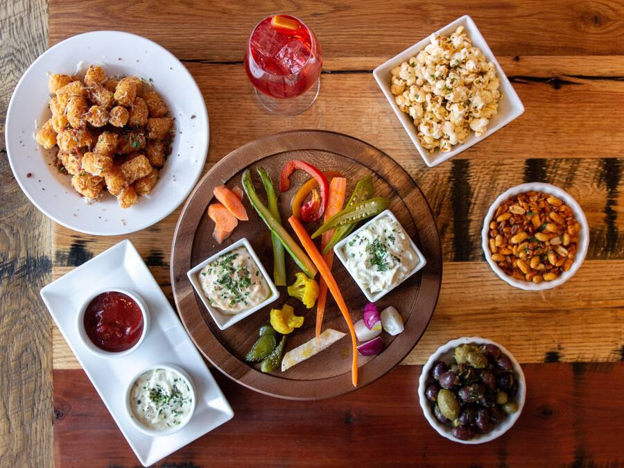 A wooden table with a variety of food items including tater tots, popcorn, and dips.