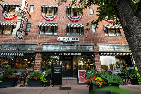 The exterior of the Armstrong Hotel with a brick facade, American flags, and a classic storefront design.