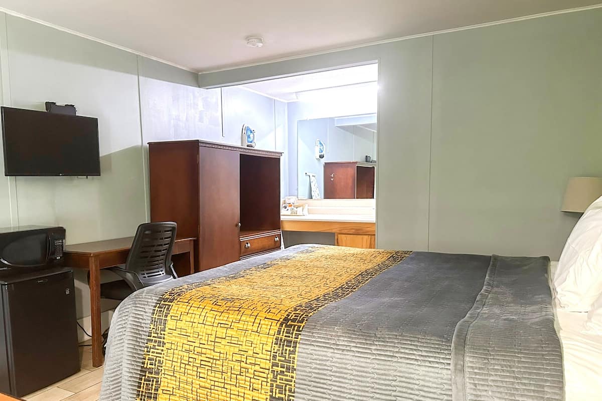 Une chambre d’hôtel équipée d’un lit, d’un bureau, d’une chaise, d’une télévision et d’un petit réfrigérateur.
