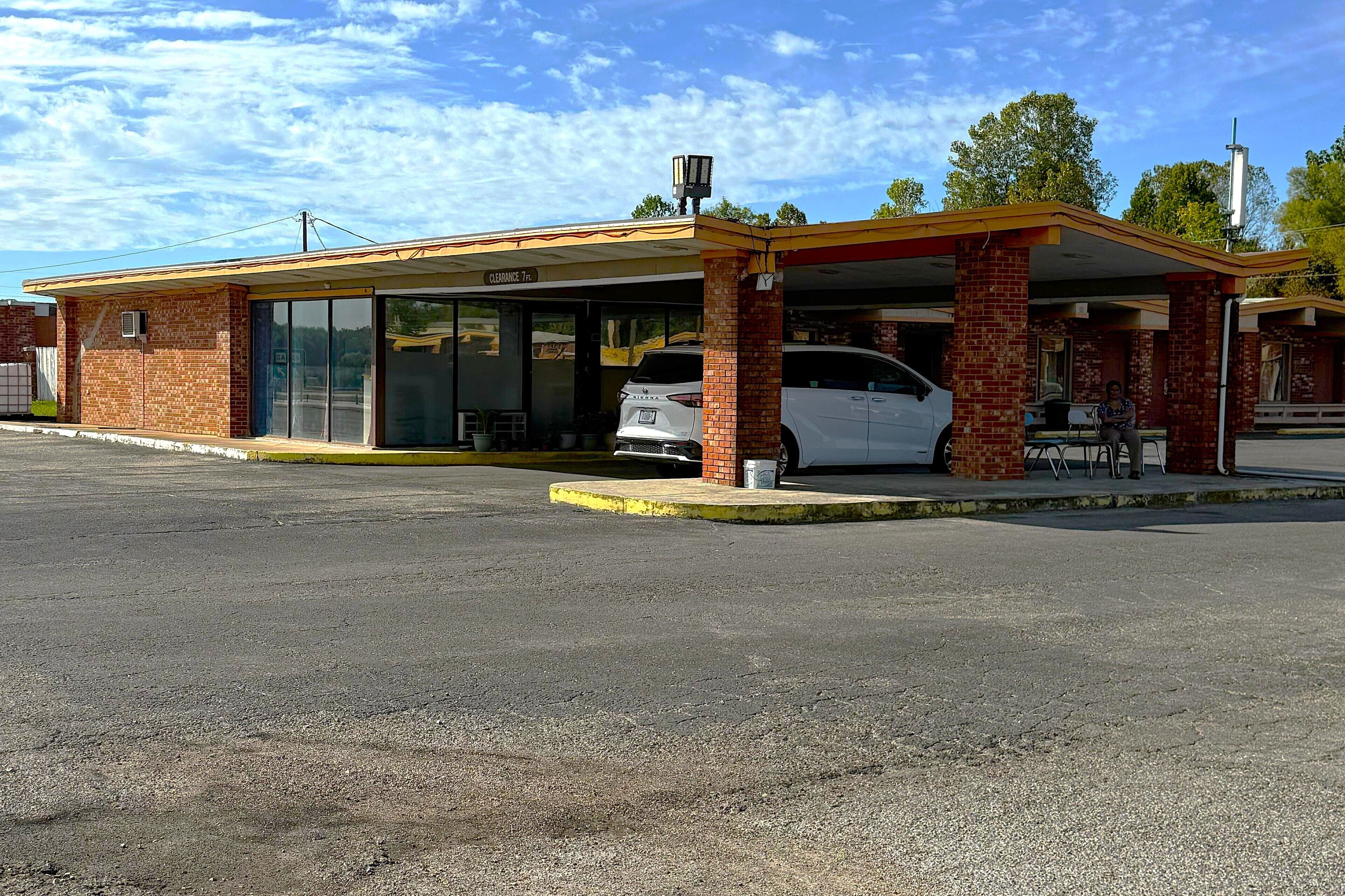 A small, single-story building with a covered parking area, a visible entrance, and a white van parked inside.