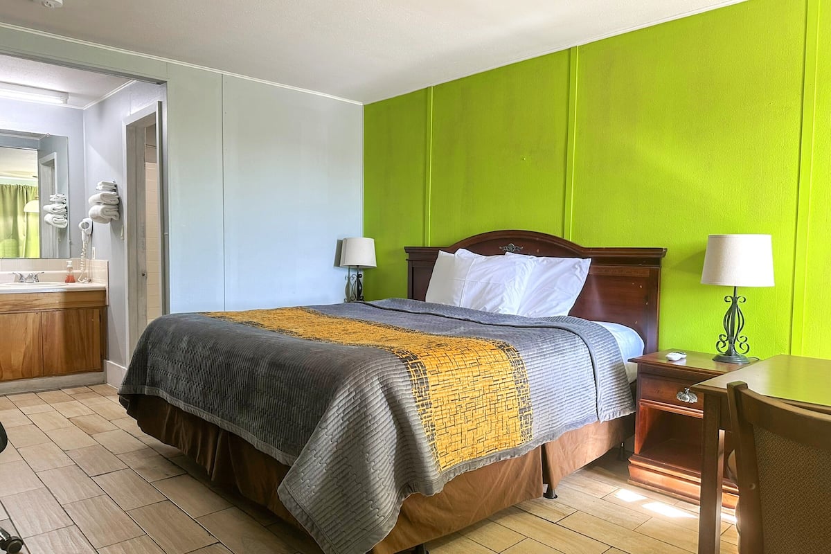 Une chambre d’hôtel avec un lit, des tables de chevet, un bureau et une salle de bain visible à travers une porte ouverte.
