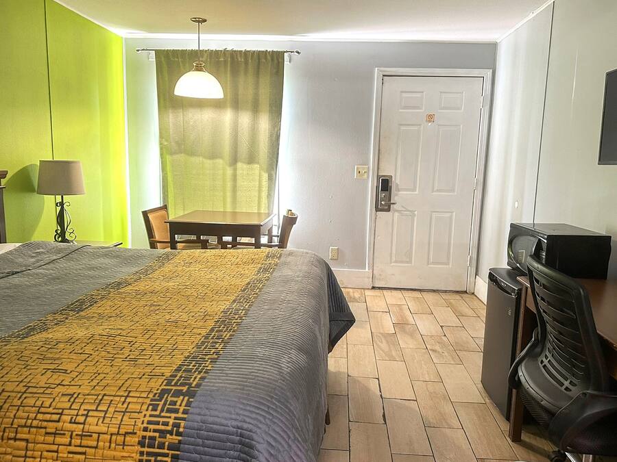 Ett hotellrum med en säng, ett skrivbord, en stol, en tv och en dörr.