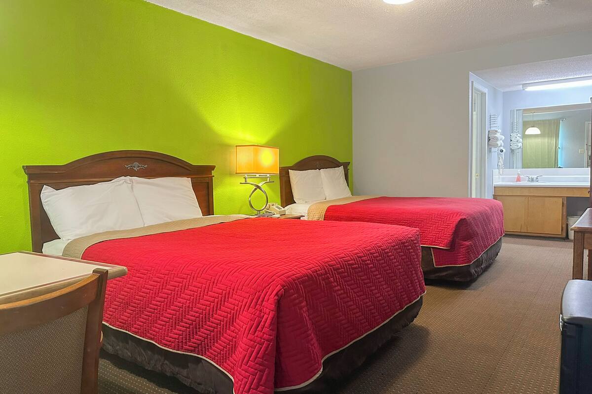 Une chambre d’hôtel avec deux lits, chacun recouvert d’une courtepointe rouge matelassée, doté d’une tête de lit en bois et agrémenté d’une table de chevet avec une lampe.
